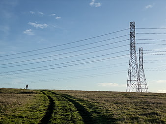 Hiker walking on grassy hill with power lines