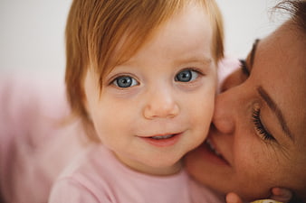 Close-up of mother kissing smiling baby girl on cheek
