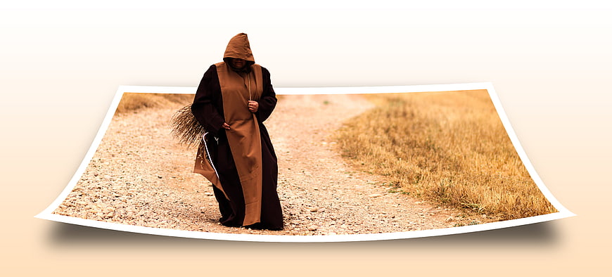 Monk in brown habit walking on dirt road with broom