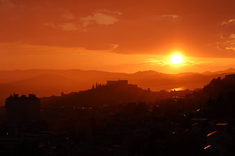 Vibrant orange sunset over silhouetted mountain cityscape