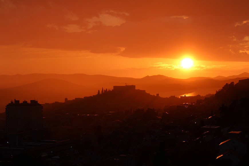 Vibrant orange sunset over silhouetted mountain cityscape