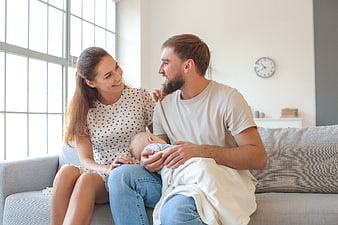 Happy Young Parents Holding Newborn Baby on Sofa