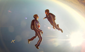 Two skydivers in free fall with airplane and sun flare