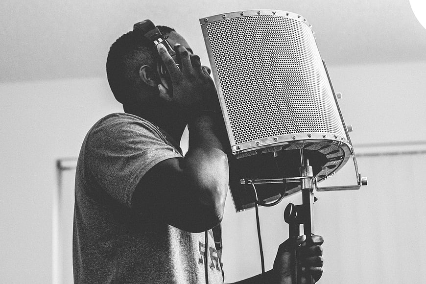 Black and white photo of a man singing into a studio microphone