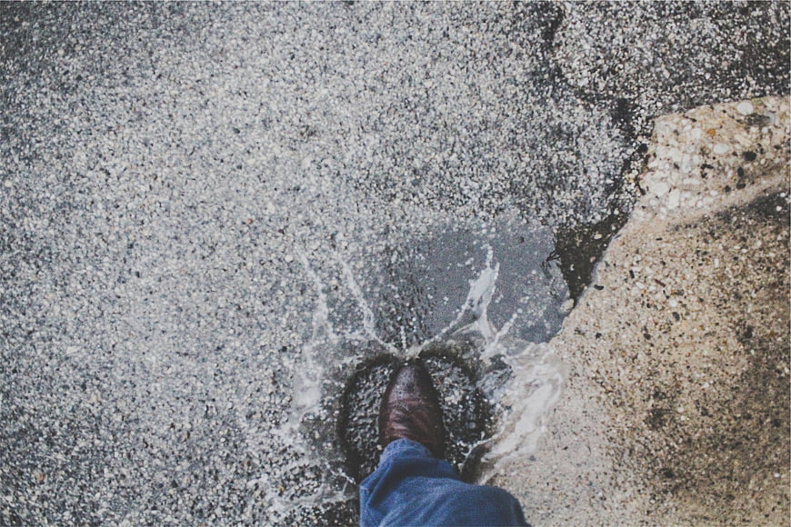 First-person view of brown leather shoe splashing in puddle