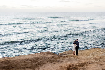 Couple embracing on rocky cliff overlooking vast ocean waves