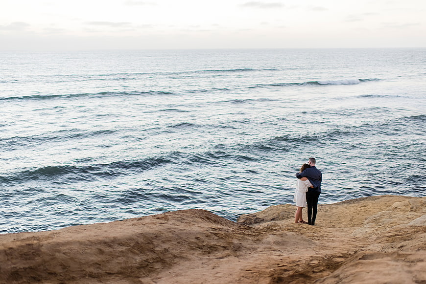 Couple embracing on rocky cliff overlooking vast ocean waves