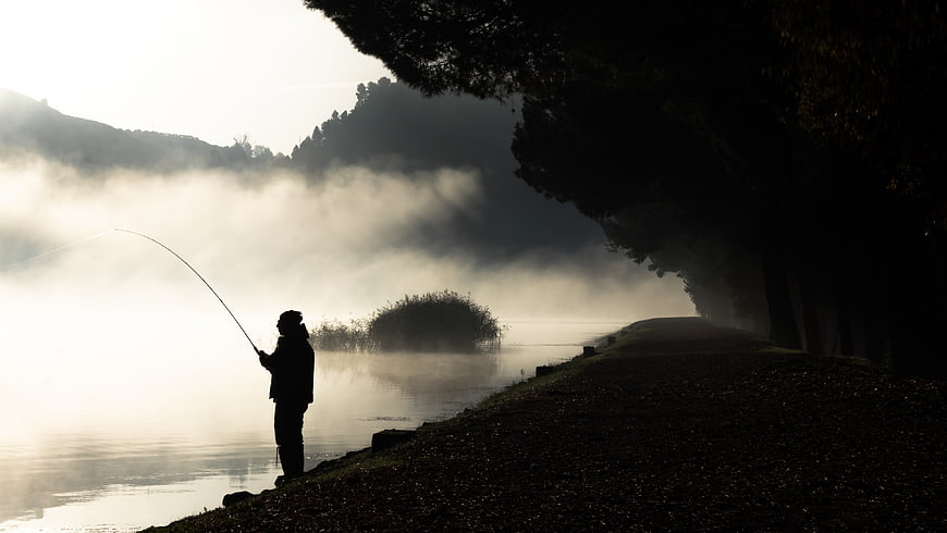 Silhouette of fisherman on misty river bank at dawn