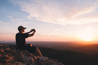 Man taking photo of sunset from mountain peak