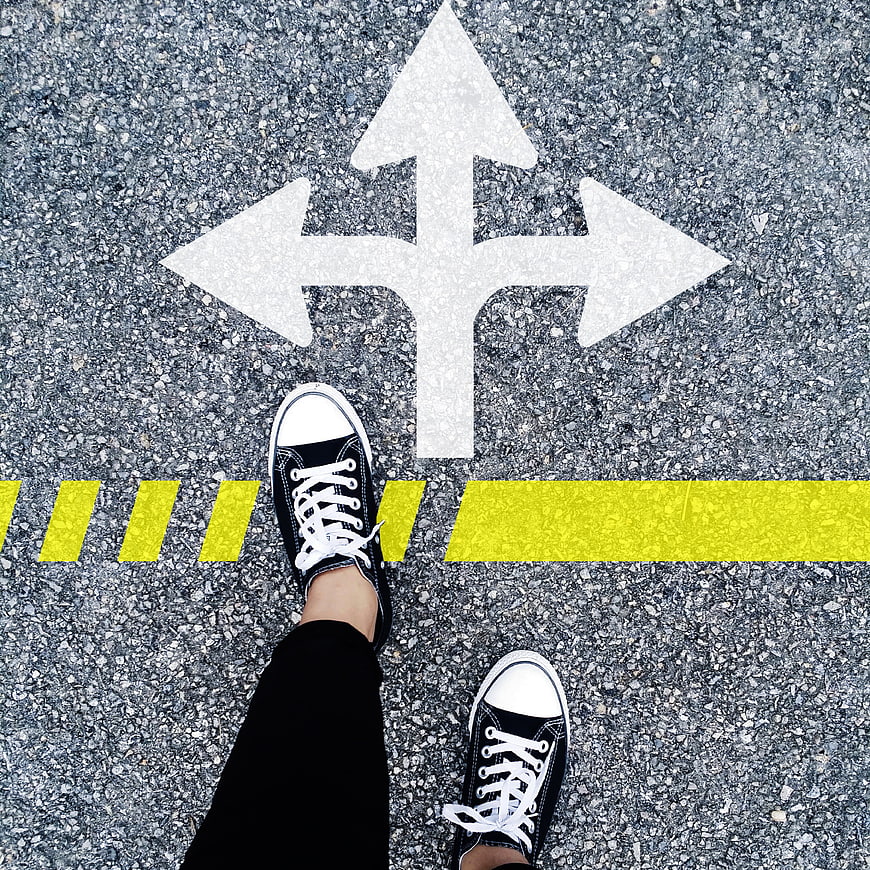 Person standing at crossroads with directional arrows on asphalt