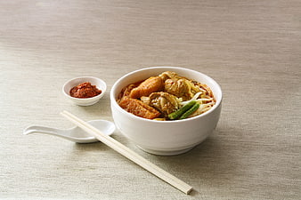 Bowl of spicy laksa noodle soup with chicken and chili paste