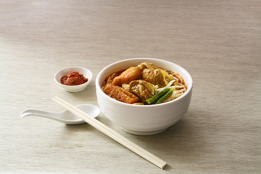 Bowl of spicy laksa noodle soup with chicken and chili paste