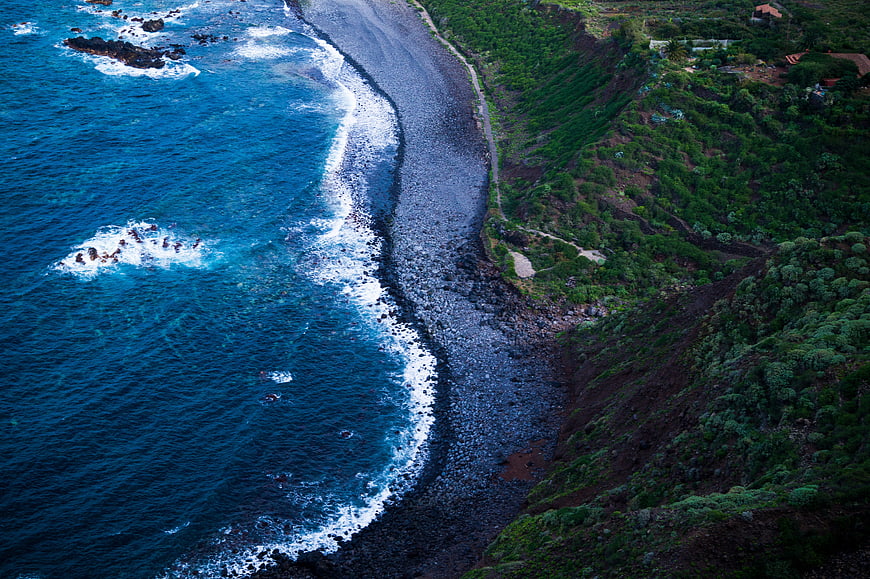 Aerial view of black pebble beach with turquoise waves and green cliffs