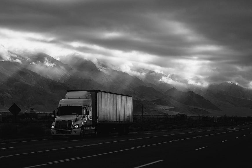 Black and white semi-truck driving on highway with dramatic mountains