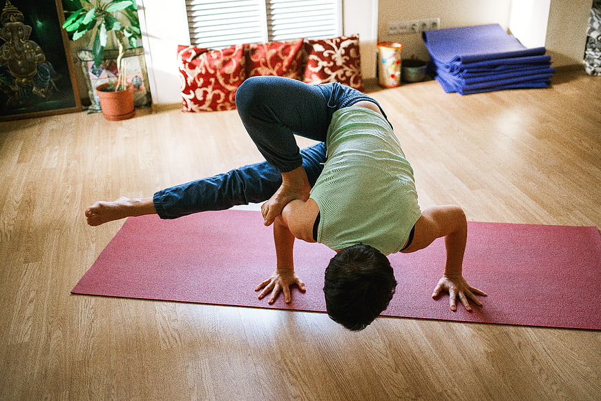 Man performing advanced yoga arm balance pose indoors