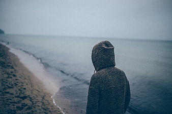 Lone figure in hoodie looking out at misty ocean beach