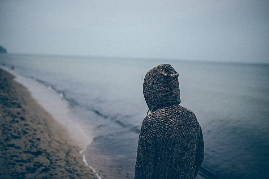 Lone figure in hoodie looking out at misty ocean beach
