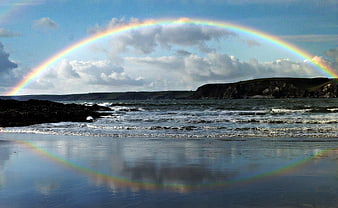 Vibrant Rainbow Arching Over Coastal Beach with Reflection