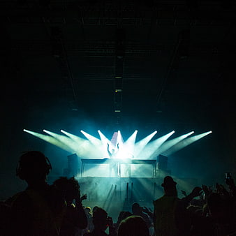 DJ Silhouette on Stage with Blue Spotlights and Crowd