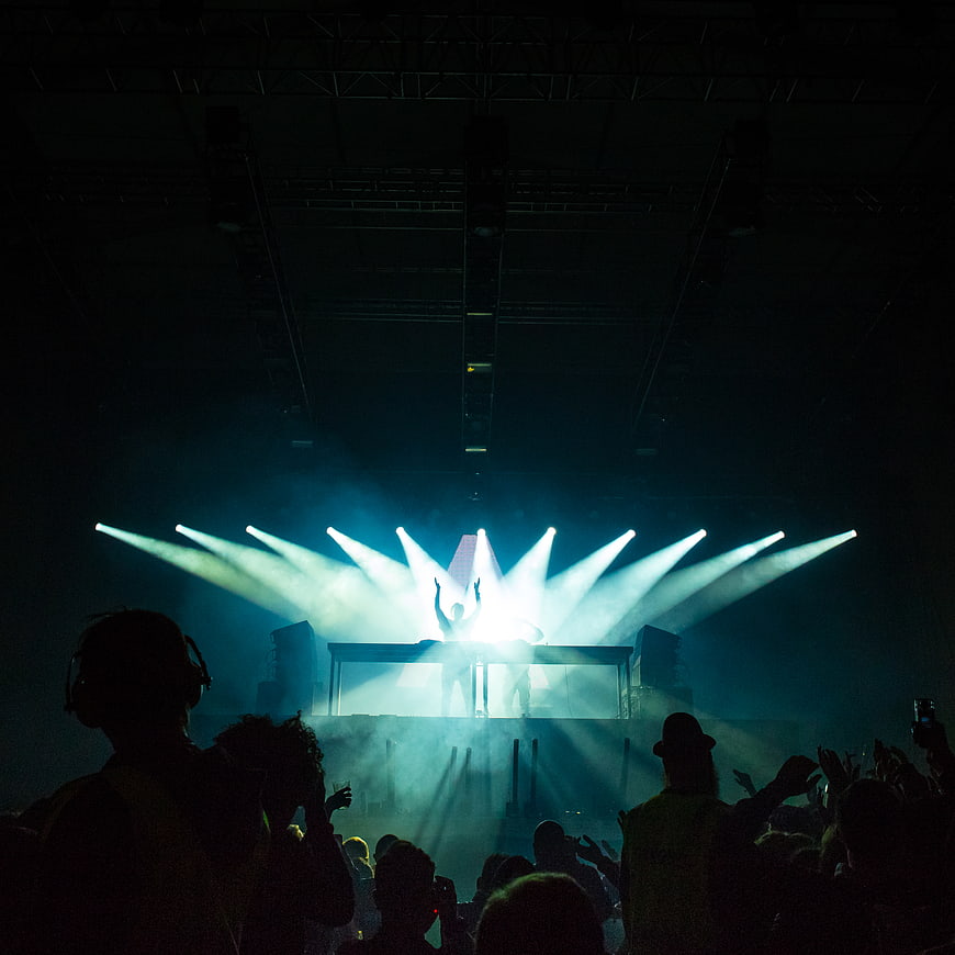 DJ Silhouette on Stage with Blue Spotlights and Crowd
