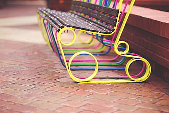 Colorful metal bench with wooden slats on brick pavement