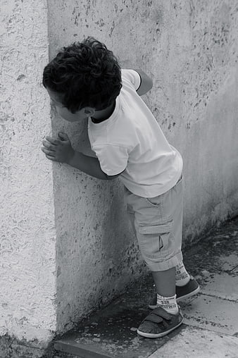 Young boy peeking around corner of textured concrete wall in black and white
