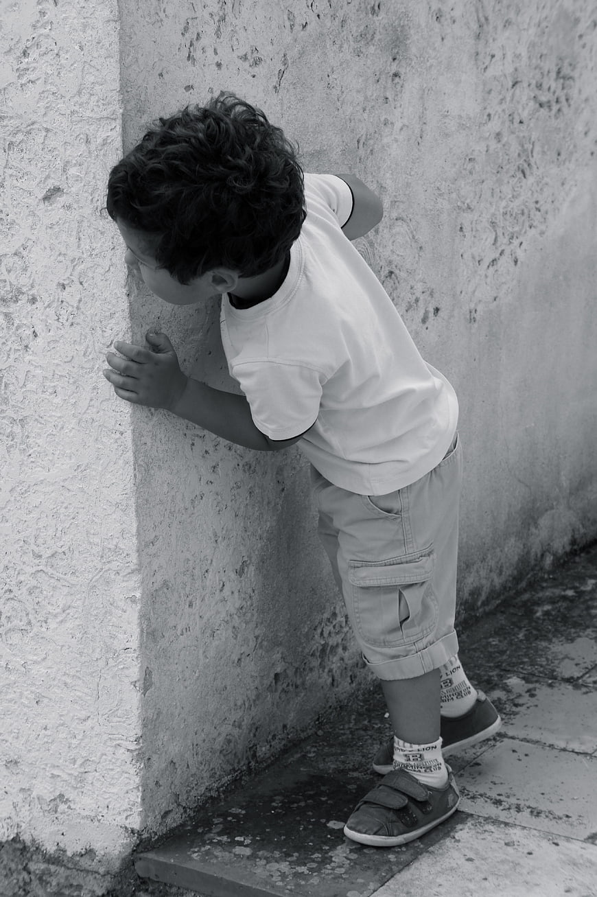 Young boy peeking around corner of textured concrete wall in black and white