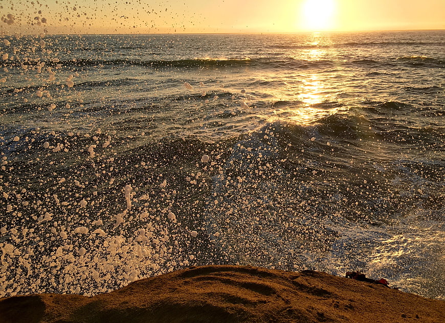 Ocean waves crashing on rocks at golden sunset