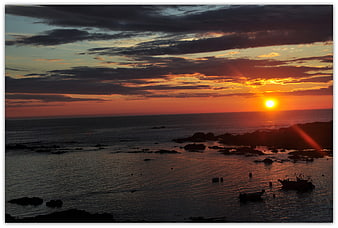 Dramatic sunset over rocky coastline with silhouetted boats