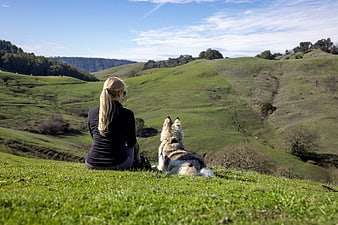 Woman and Dog Sitting on Green Hillside