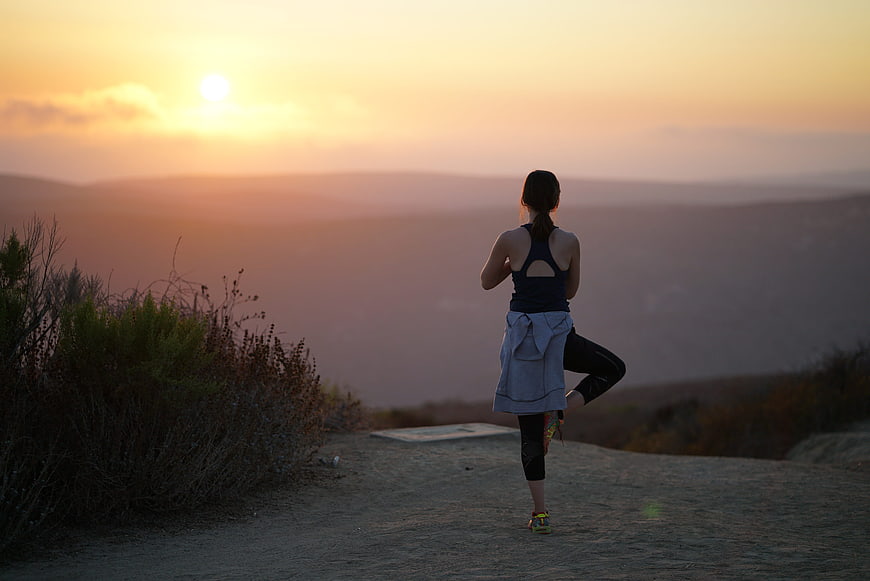 Woman practicing yoga tree pose on a hilltop at sunset