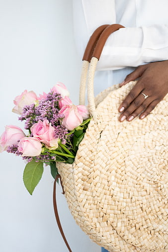 Woman holding woven straw bag with pink roses and purple flowers