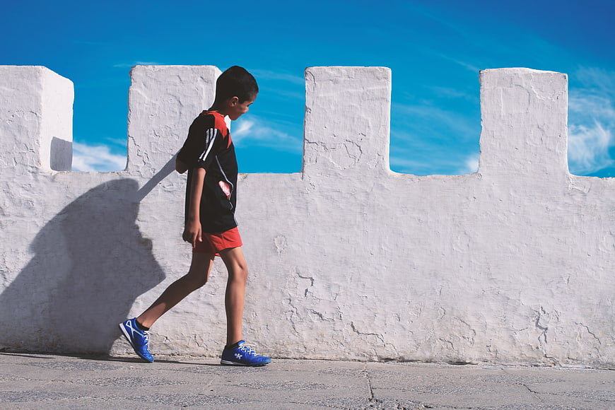 Young boy walking past white wall under blue sky