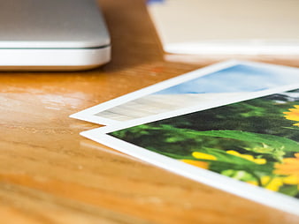 Close-up of printed photos on wooden desk with laptop