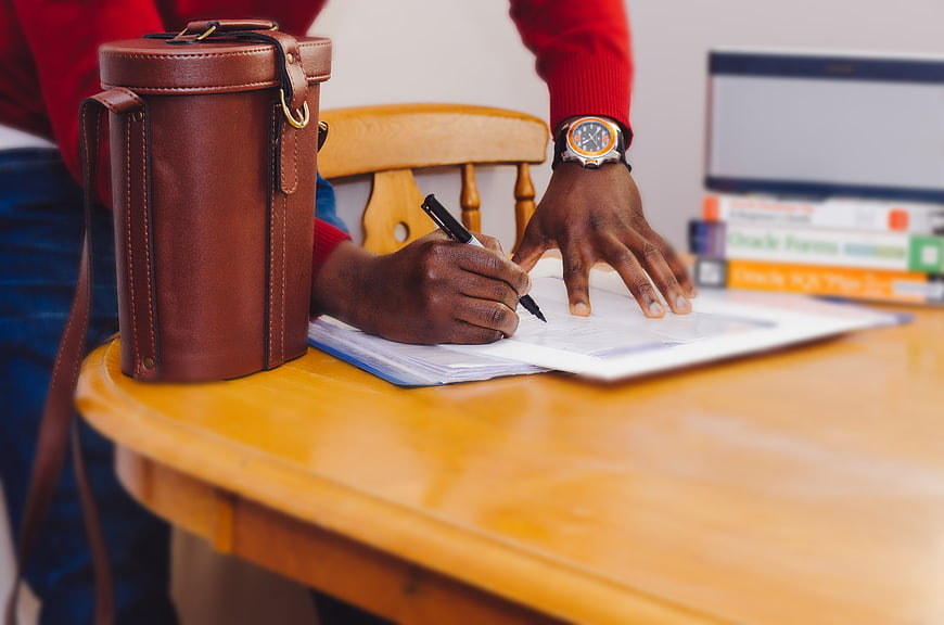 Man writing at wooden desk with leather bag and books