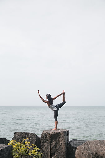 Woman doing yoga pose on rocks by the ocean