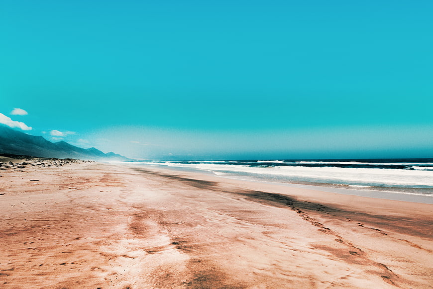 Wide sandy beach with turquoise sky and ocean waves