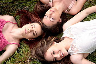 Three young women lying in grass forming a circle