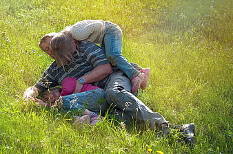 Father wrestling with two daughters in sunny meadow