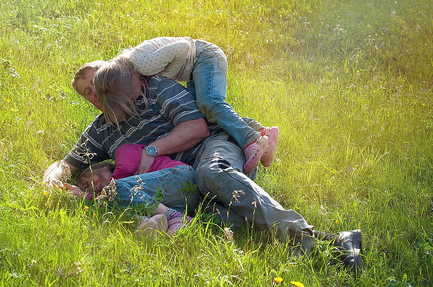Father wrestling with two daughters in sunny meadow
