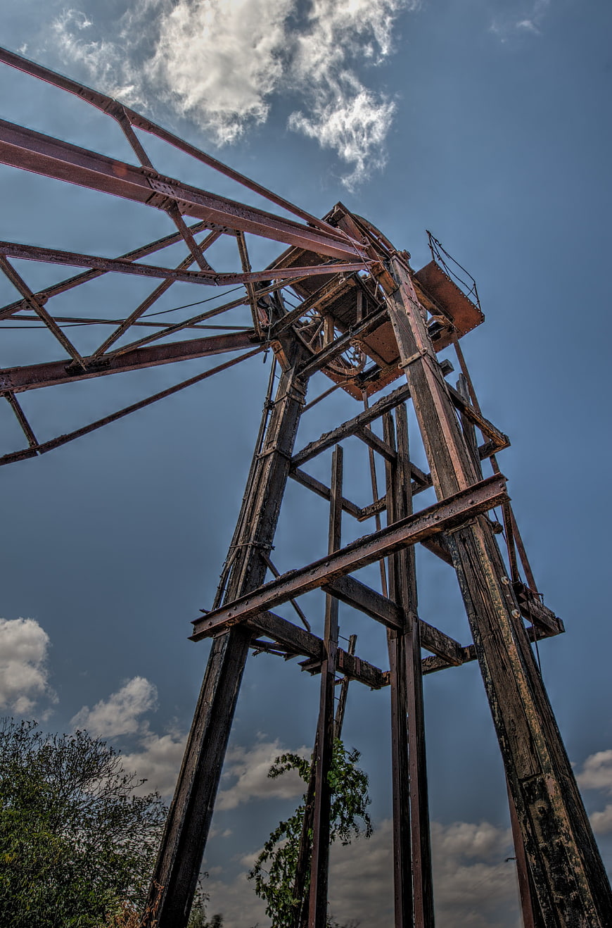 Low angle view of rusty industrial mining headframe against blue sky