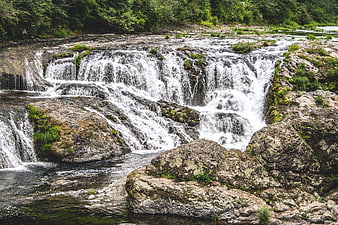 Wide cascading waterfall flowing over rocky terrain in a forest