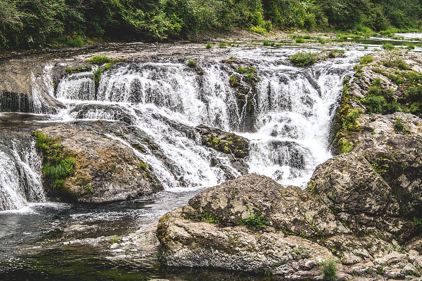 Wide cascading waterfall flowing over rocky terrain in a forest