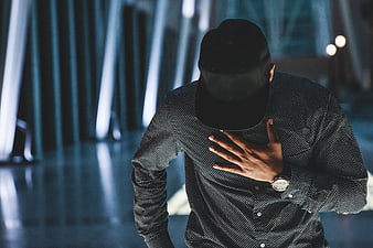Man in Black Cap and Patterned Shirt with Hand on Chest
