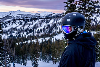 Skier in Helmet Looking at Snowy Mountain Landscape at Dusk