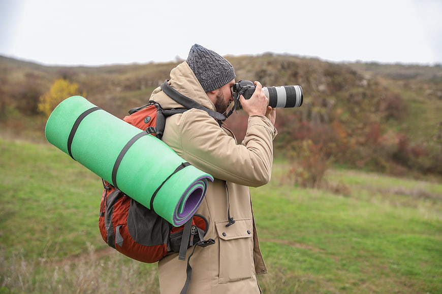 Male Hiker With Backpack And Telephoto Camera In Autumn Landscape
