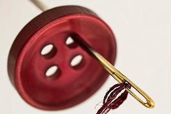 Close-up of brass needle with thread through red button