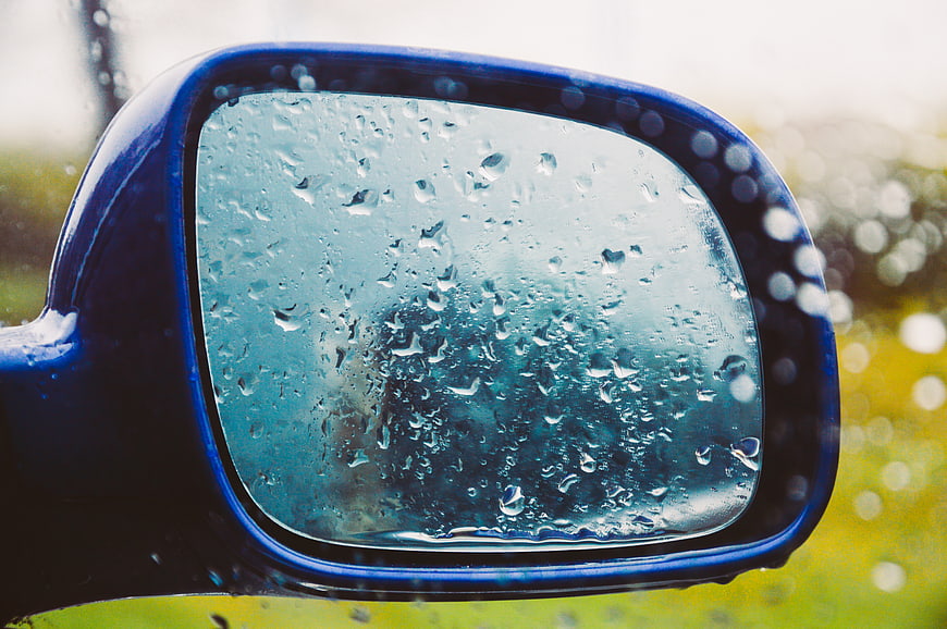 Close-up of blue car side mirror with raindrops