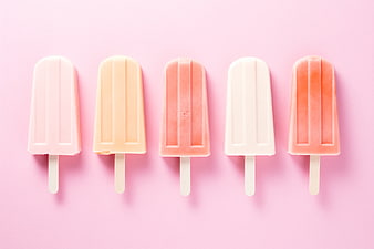 Colorful pastel popsicles arranged in a row on pink background