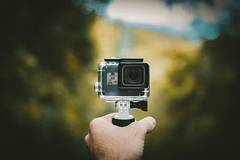 Hand holding action camera with blurred nature background